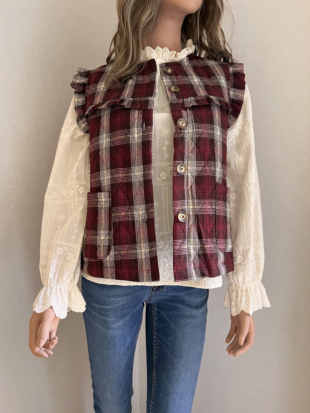 Gilet Victor sans manches à carreaux bordeaux et écru, vue de face sur une blouse brodée écrue | Coka Collection
