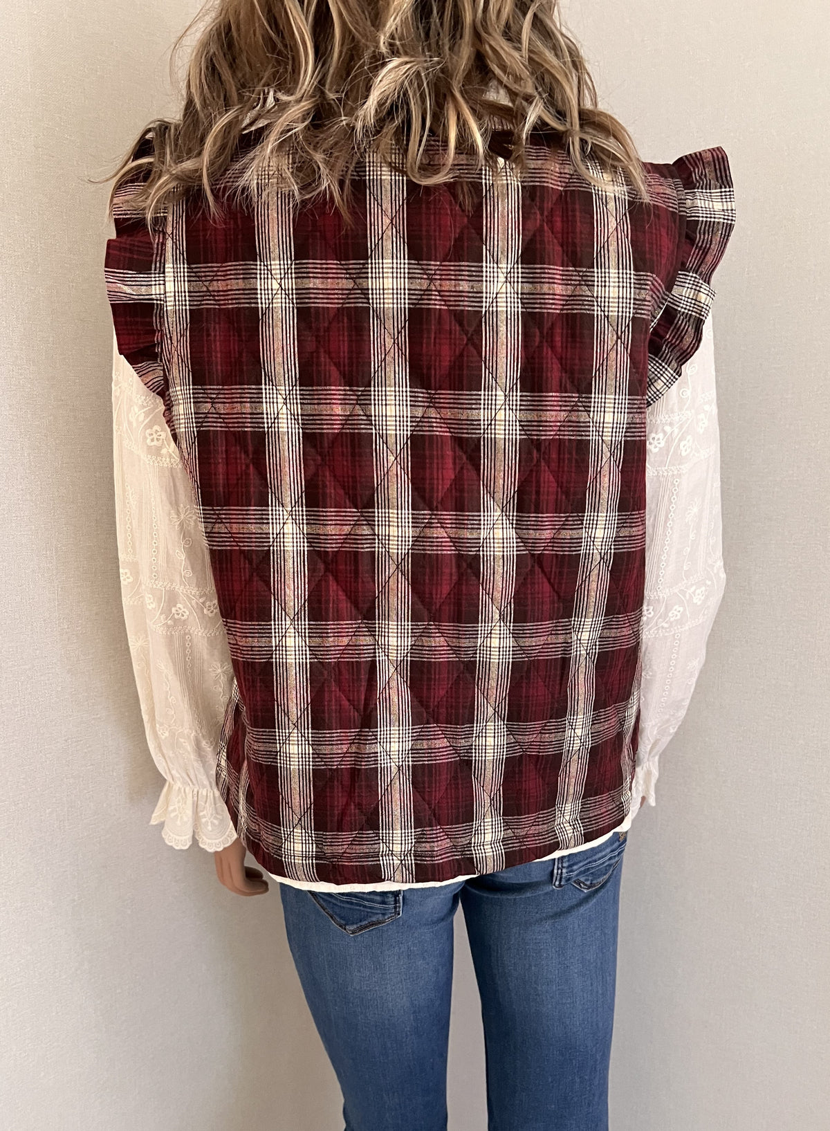 Gilet Victor sans manches à carreaux bordeaux et écru, vue de dos sur une blouse brodée | Coka Collection